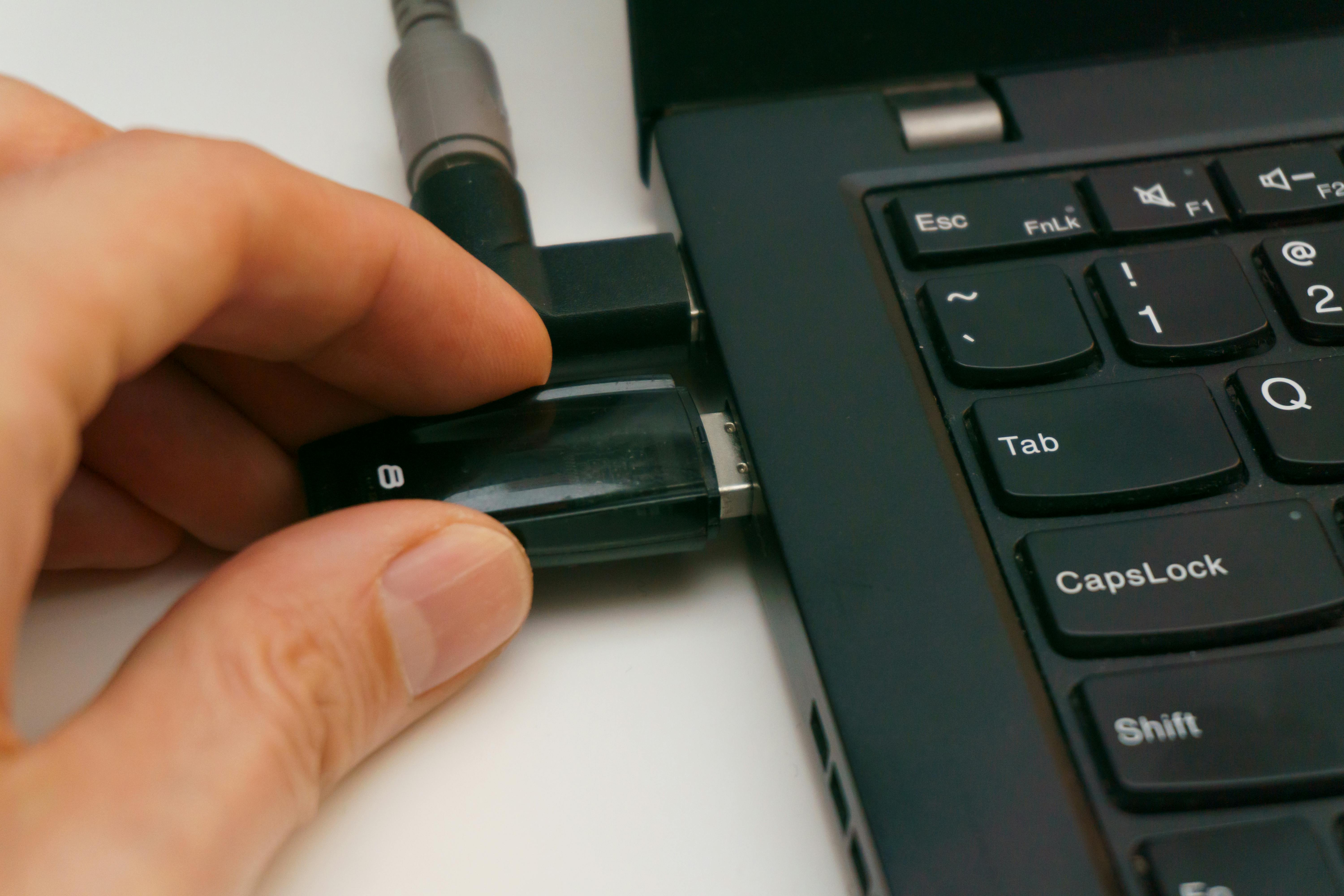 A close-up of a hand inserting a USB drive into a laptop port, highlighting technology and connectivity.